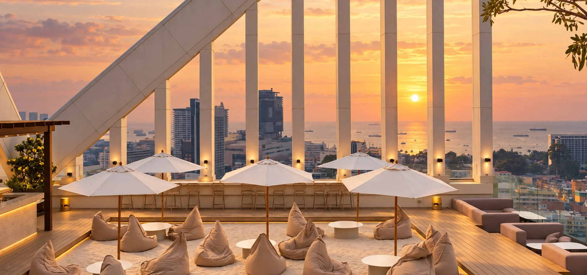 Sunset over the sea from the rooftop bar of Arbour Hotel and Residence Pattaya, with sand lounge, white umbrellas and city views